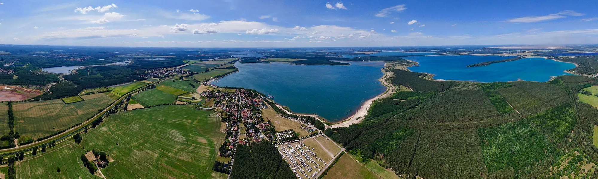 Luftbild des Geierswalder Sees mit dem Ort Geierswalde, dem Ferienpark und dem Strand am Ostufer